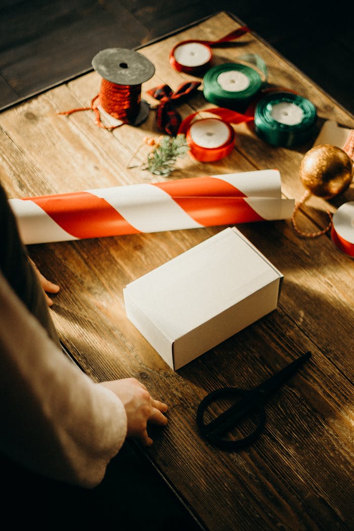 A warm depiction of gift wrapping with ribbons, scissors, and decorations on a wooden table.